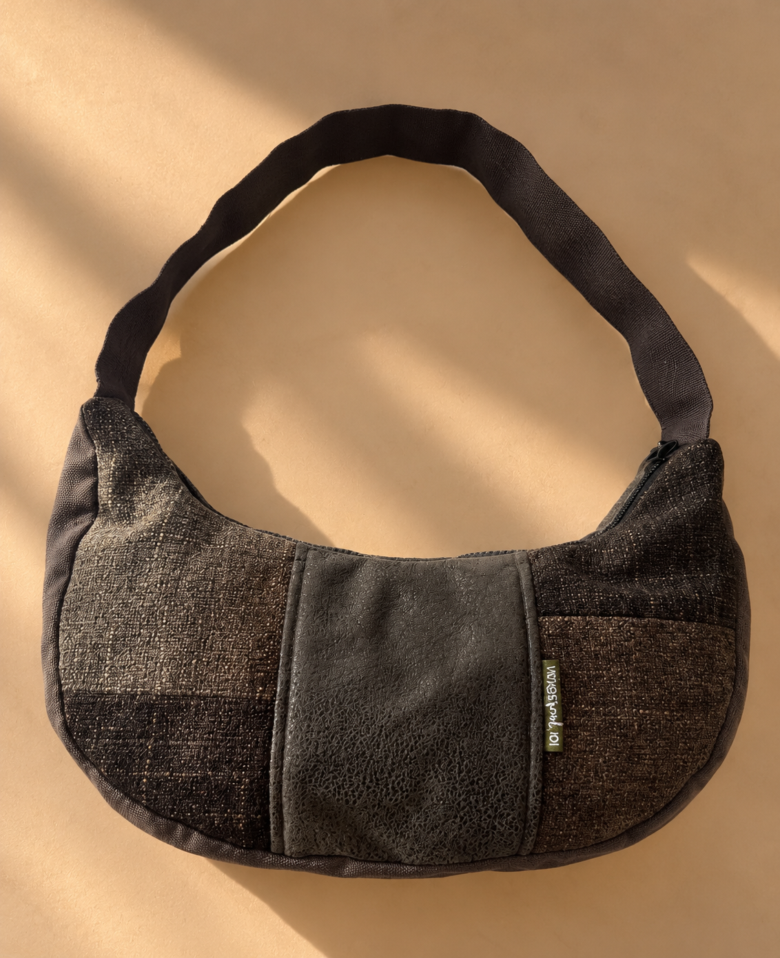 Charcoal and bronze-toned patchwork crescent shoulder bag with textured side panels, a dark centre panel and dark shoulder strap.
