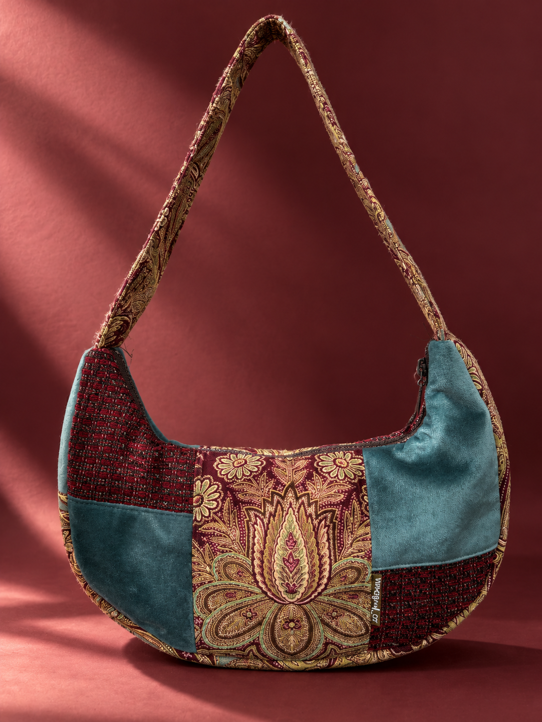 Teal and burgundy patchwork shoulder bag with a gold-toned floral and paisley centre panel, textured burgundy patches and a patterned strap.