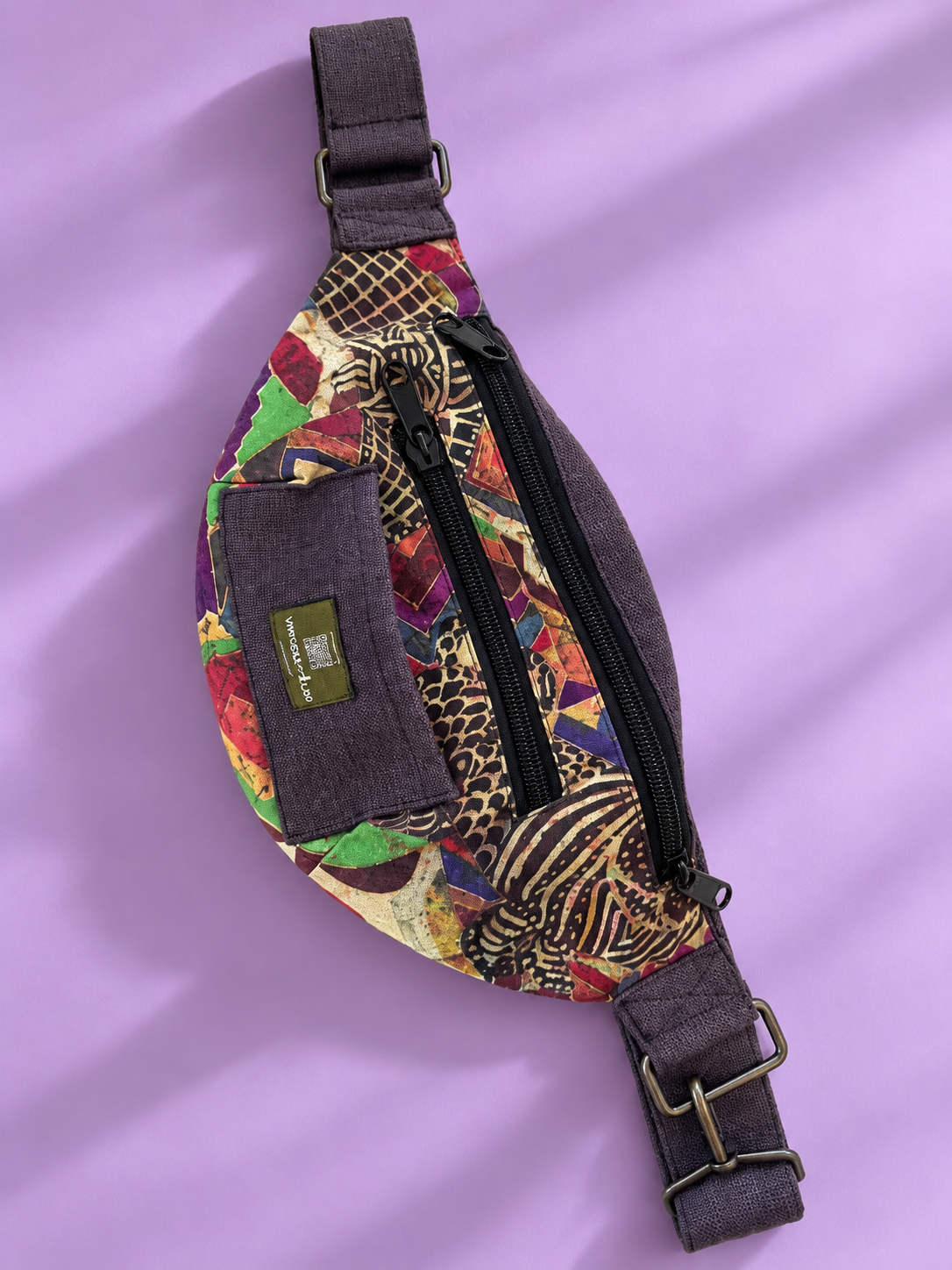 Colorful patchwork sling bag with dark trim on a lavender background