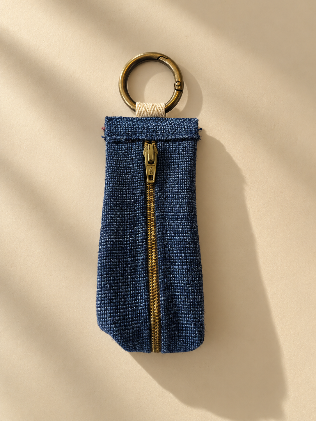 Navy-blue textured keychain pouch with a brass-tone zipper and metal key ring