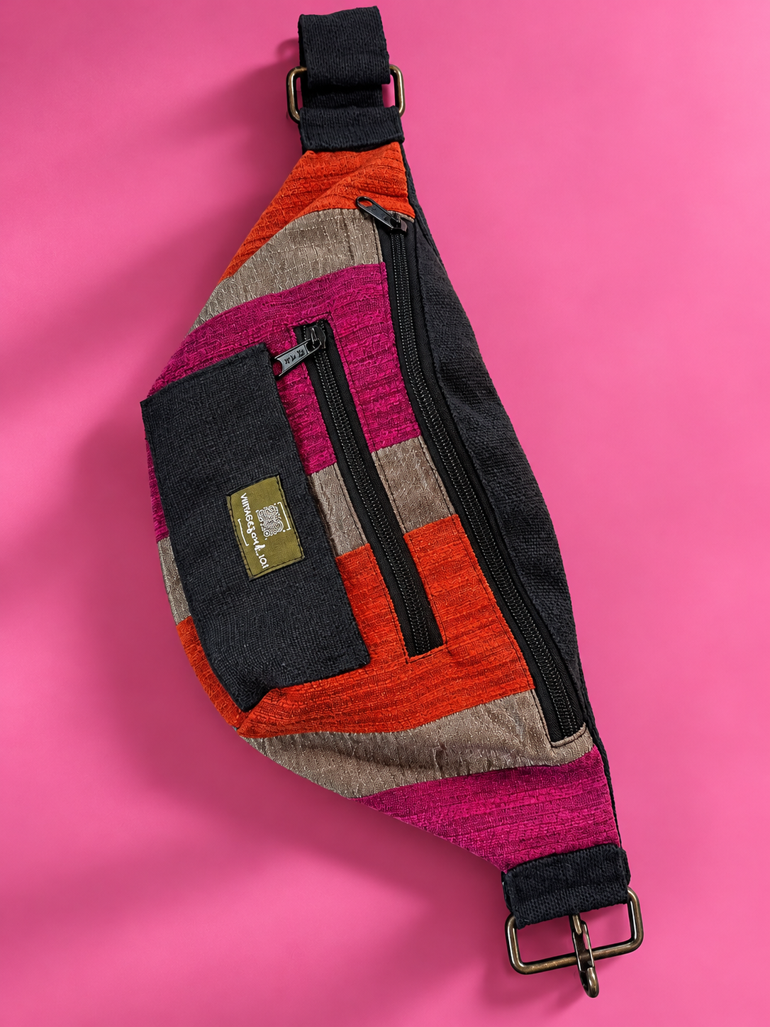 Orange, pink, and taupe crescent belt bag with black trim on a pink background