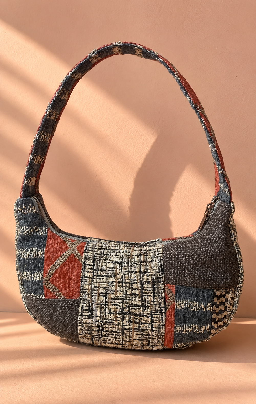 Charcoal, cream, navy and rust-orange patchwork shoulder bag with a textured woven centre, geometric motifs and patterned strap.