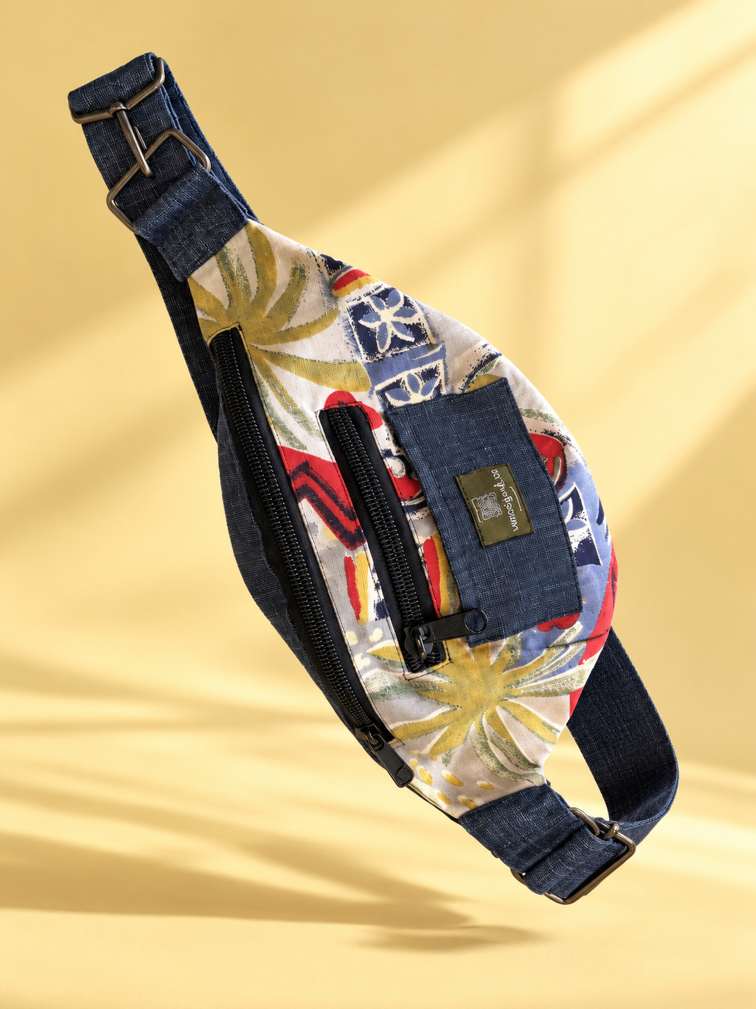 Tropical-print sling bag with dark blue trim photographed at an angle on a yellow background