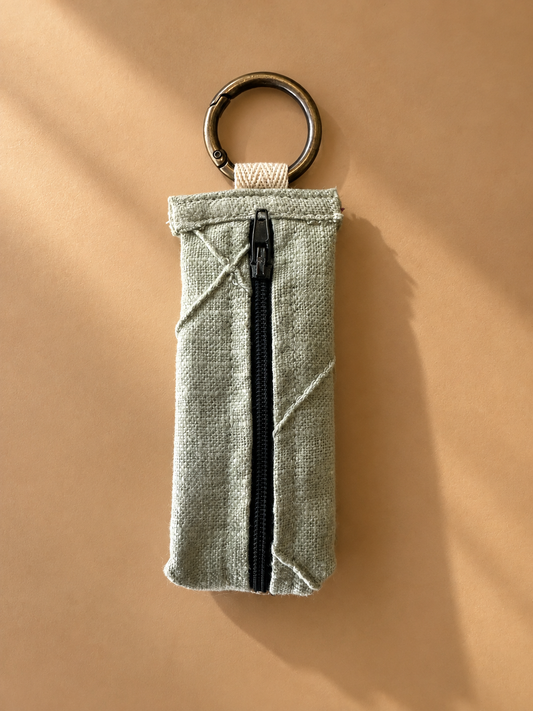 Sage-green textured keychain pouch with diagonal stitching, black zipper, and metal key ring