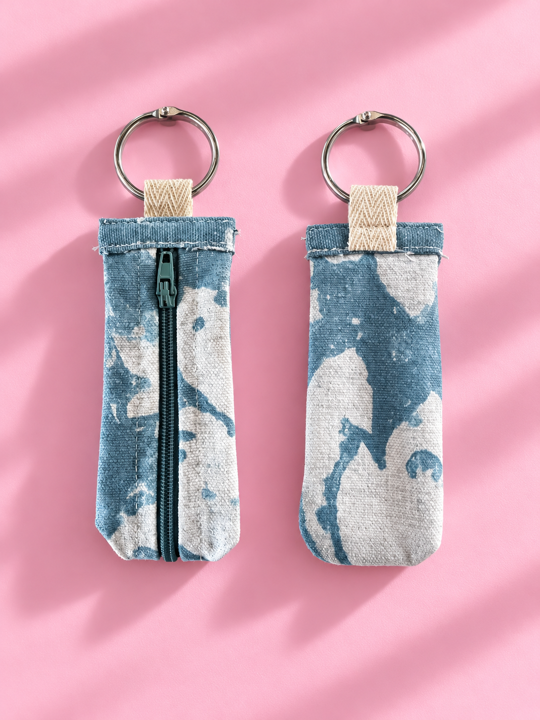 Front and back views of a soft blue and cream abstract keychain pouch with a zipper and silver-tone key ring