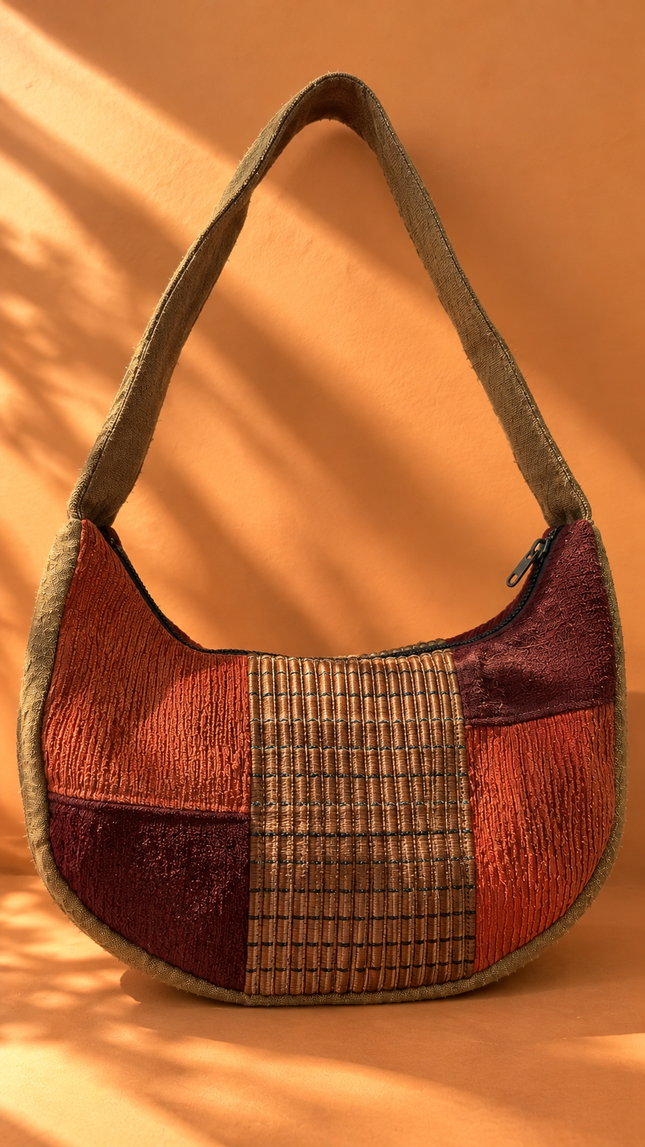 Rust-orange and burgundy patchwork crescent bag with a tan vertically striped centre panel and olive-brown shoulder strap and trim.