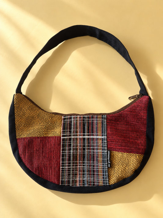 Burgundy and mustard patchwork crescent bag with a multicoloured plaid centre panel, black shoulder strap and black edging.