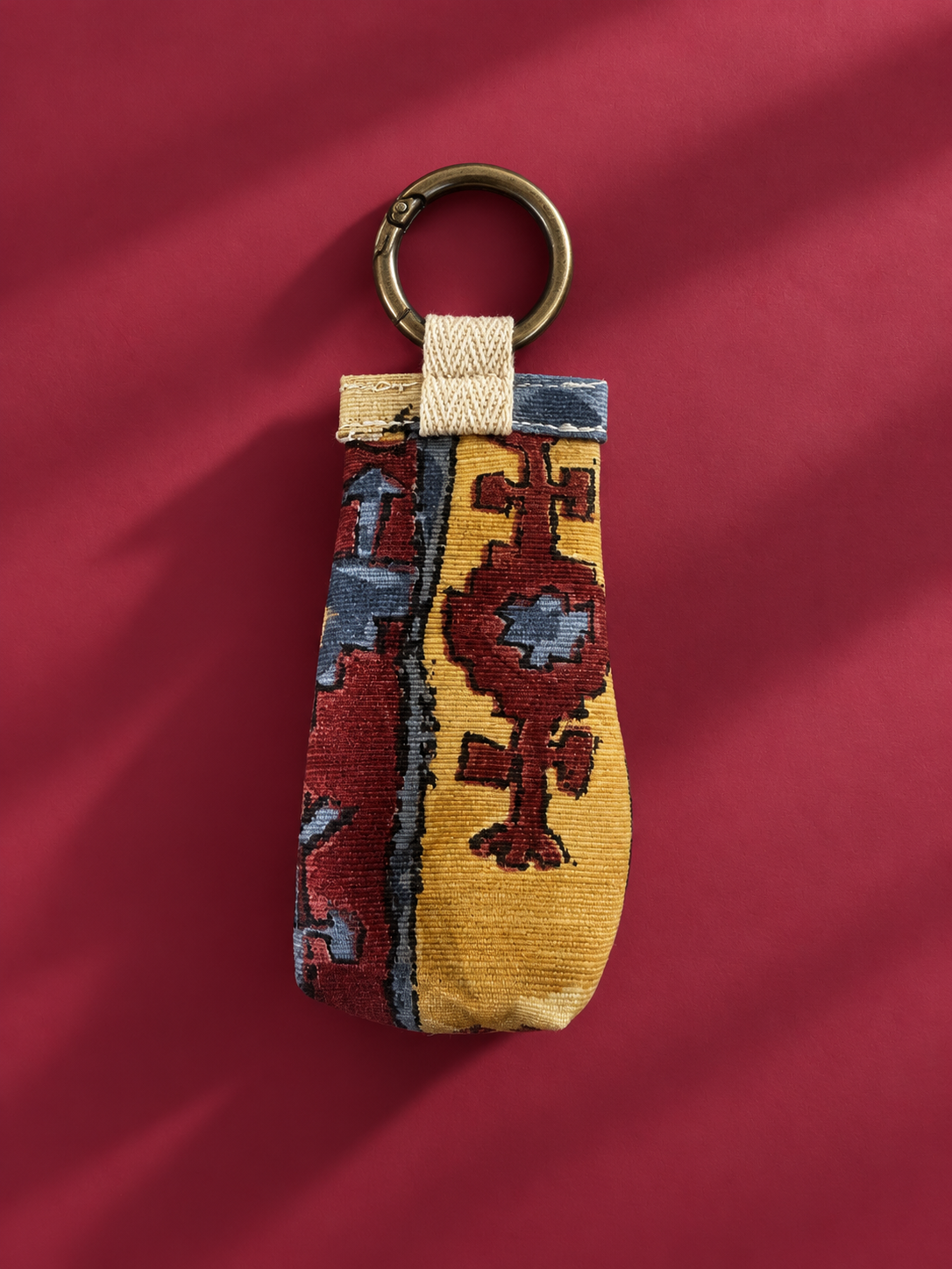 Front of upcycled tapestry keychain pouch in mustard, burgundy, and blue