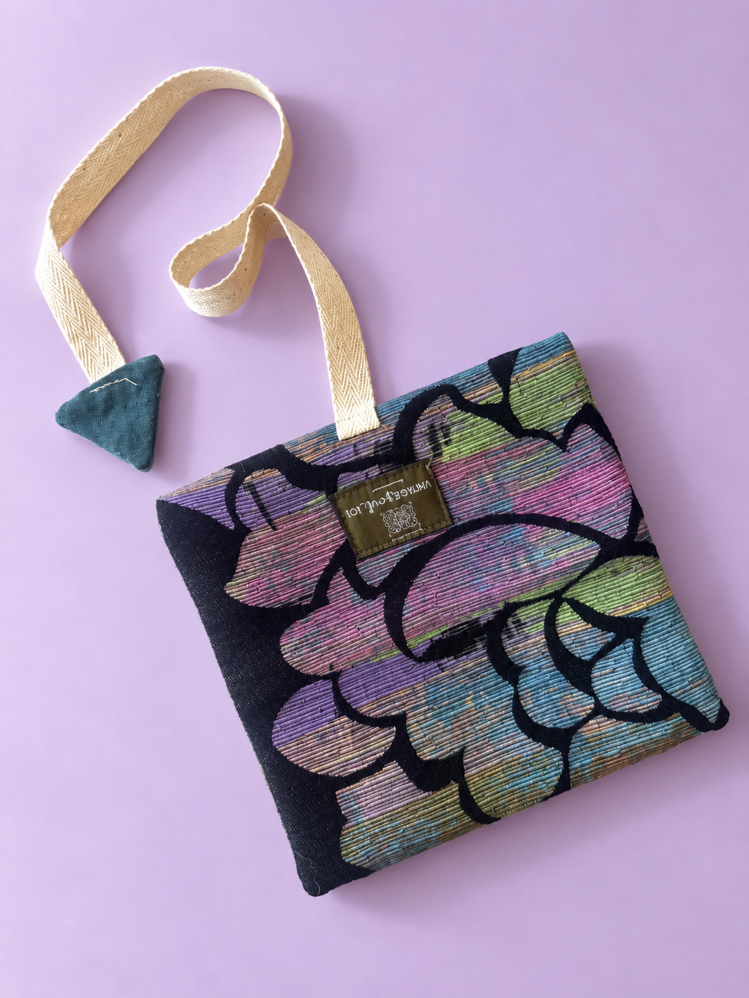 Pastel floral tapestry pouch with black outlines, cream woven strap and slate blue triangular detail