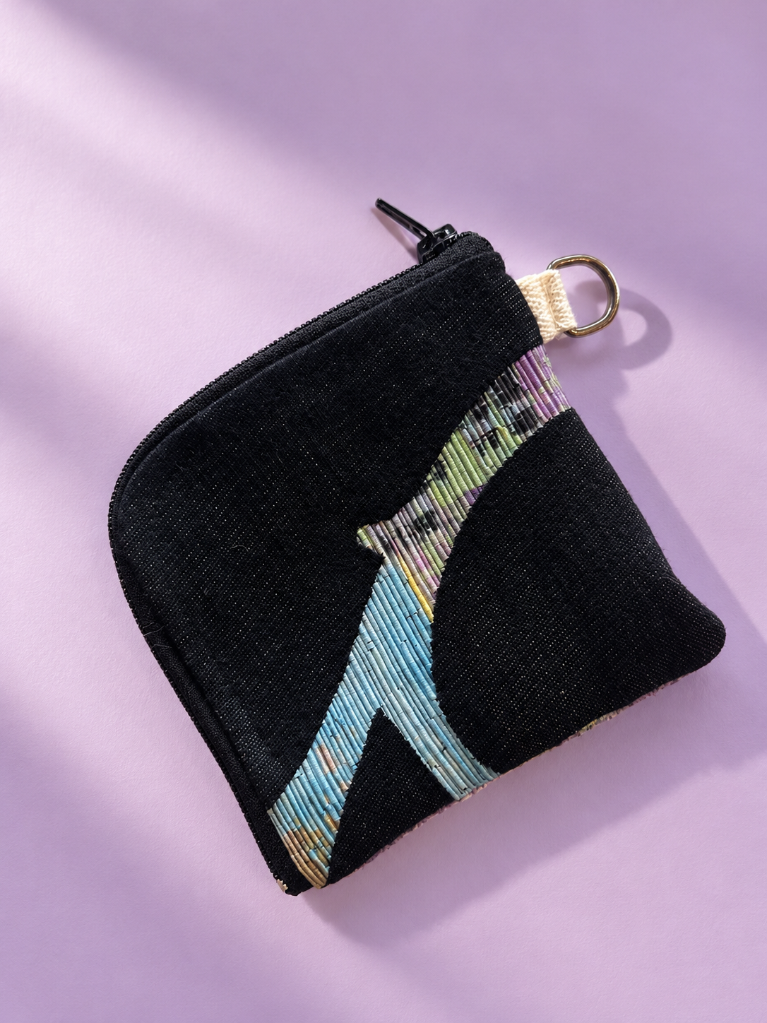 Black textured zip pouch with pastel-striped patchwork and a gold-tone side ring