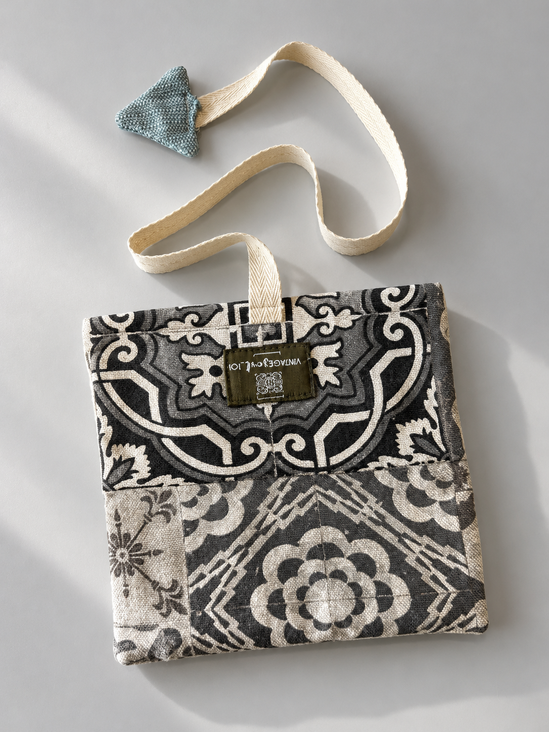 Black, grey and cream patterned pouch with cream woven strap and teal triangular detail