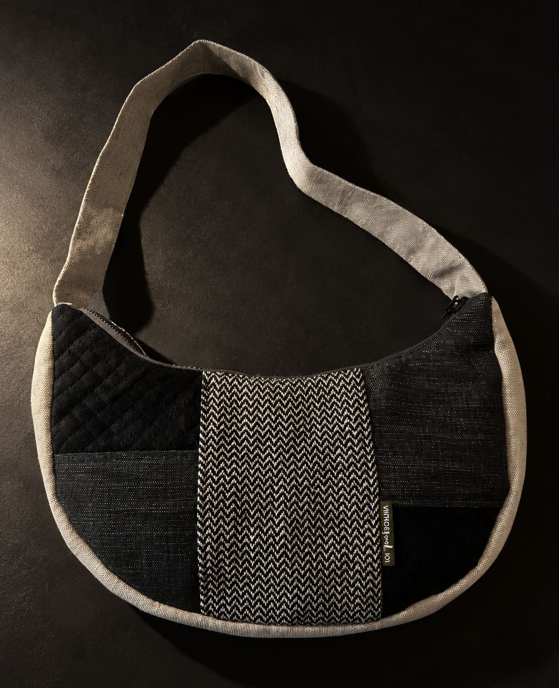 Black and charcoal patchwork crescent shoulder bag with a black-and-cream zigzag centre panel and cream strap and trim.