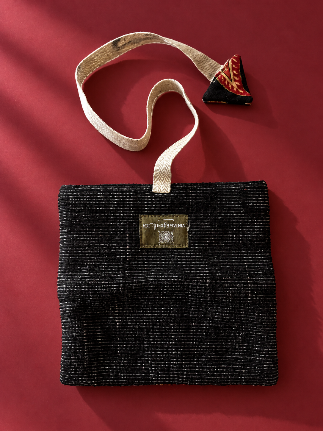 Black textured pouch with cream woven strap and paisley triangular detail