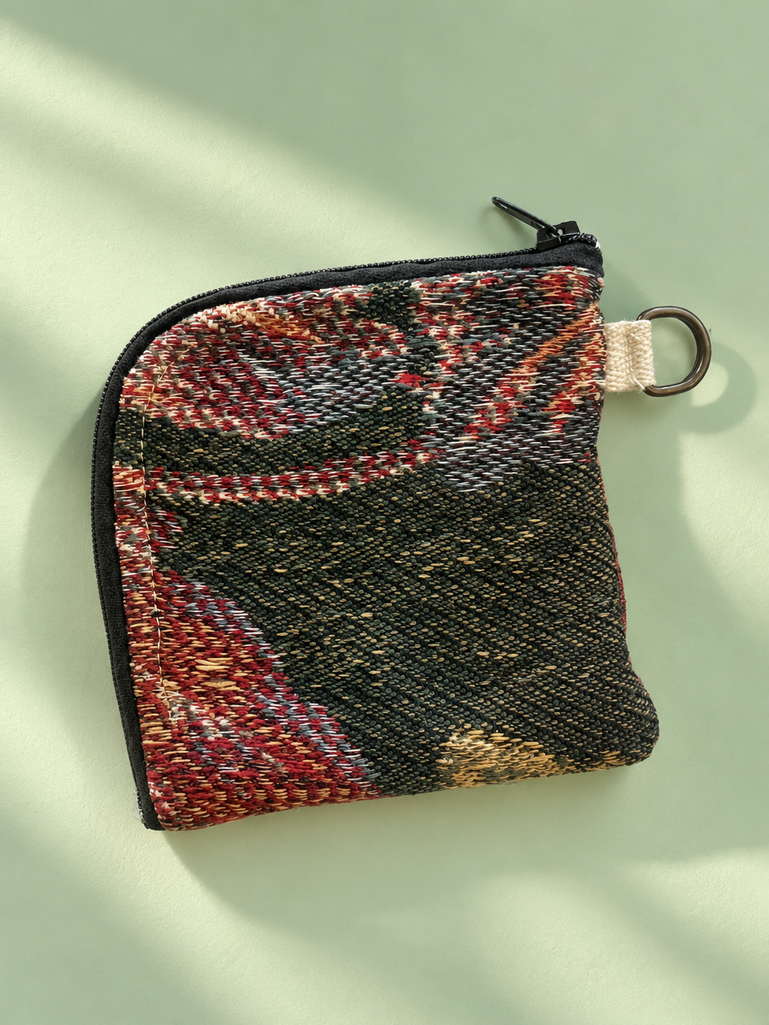 Woven tapestry-patterned zip pouch in dark green, rust and cream with black zipper and metal side ring