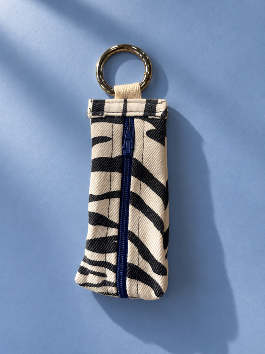 Black and cream zebra stripe keychain pouch with a blue zipper and metal key ring